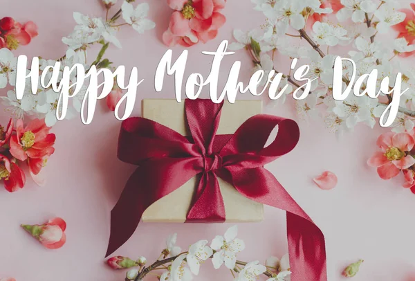 Anneler Günün kutlu olsun. Mutlu anneler günü mesajı ve pembe arka planda kırmızı ve beyaz çiçekli hediye kutusu. Şık bir çiçek tebrik kartı. El yazısıyla yazılmış harfler. Anneler Günü