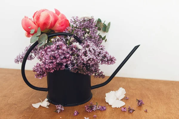 Güzel şakayık, leylak çiçekleri ve okaliptüs, taşra arka planında kaliteli metal sulama düzenlenebilir. Anneler Günün kutlu olsun ya da Sevgililer Günü. Merhaba bahar. Modern çiçekler hala hayat