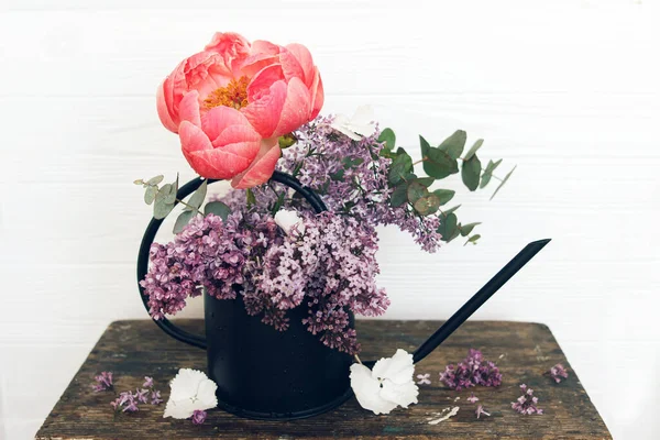 Güzel şakayık, leylak çiçekleri ve okaliptüs, şık metal sulama kabında. Merhaba bahar. Kırsal ahşap arka planda modern çiçekli natürmort yaşam düzeni. Anneler günün kutlu olsun.