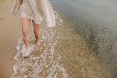 Kaygısız güzel kadın kumlu sahilde çıplak ayakla koşuyor soğuk deniz dalgalarıyla, eğleniyor. Kesik manzara. Şık, mutlu bir bayan, dinleniyor ve sahilde tatilin tadını çıkarıyor. Su sıçratan dalgalarda ayaklar