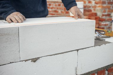 Masonluk. Otoklavla havalandırılmış beton bloklar döşeyen bir işçi. İnşaatçı beyaz blokları kapatıyor. İnşaat alanındaki ev inşaatı