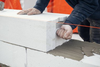 Masonluk. Otoklavla havalandırılmış beton bloklar döşeyen bir işçi. İnşaatçı beyaz blokları kapatıyor. İnşaat alanındaki ev inşaatı