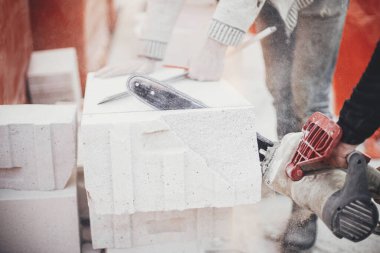 Otoklavize edilmiş beton bloğu elektrikli testereyle kesen işçiler. İnşaatçılar duvarcılık için beyaz blokları kesiyorlar. İnşaat alanındaki ev inşaatı.
