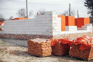 İnşaat alanında inşaat malzemeleri. Beton temeller ve tuğlalar üzerine otomatik klipslemeli bloklar, ev inşa süreci. Yatmak için beyaz hava blokları yığını.