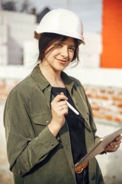 Stylish woman architect with tablet checking blueprints at construction site. Young female engineer or construction worker in hardhat looking at plans of new modern house