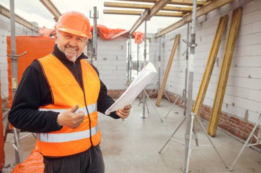 Senior male foreman in hardhat approving building new modern house according to blueprints. Portrait of happy man engineer or construction worker with plans at construction site