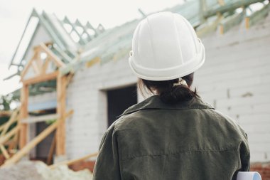 Şatafatlı bir kadın mimar inşaat alanındaki tamamlanmamış modern çiftlik evine bakıyor. Yeni modern ev planları olan genç bayan mühendis ya da inşaat işçisi.