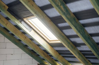 Tamamlanmamış ahşap çatı, buhar bariyeri, koğuş ve pencereleri var. Mansard 'daki beton bloklardaki kirişlere ve kirişlere bakın. Yeni modern çiftlik evi inşaatı