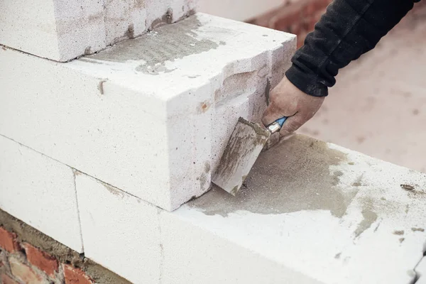 Otoklavla havalandırılmış beton bloklar döşeyen işçiler yapışkan ve malayla çalışıyorlar. İnşaatçı beyaz blokları kapatıyor. İnşaat alanındaki ev inşaatı