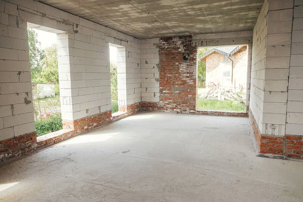 Unfinished house inside. Aerated concrete blocks wall with windows, doorways and concrete floor in sunny day. Process of house building at construction site. New house construction