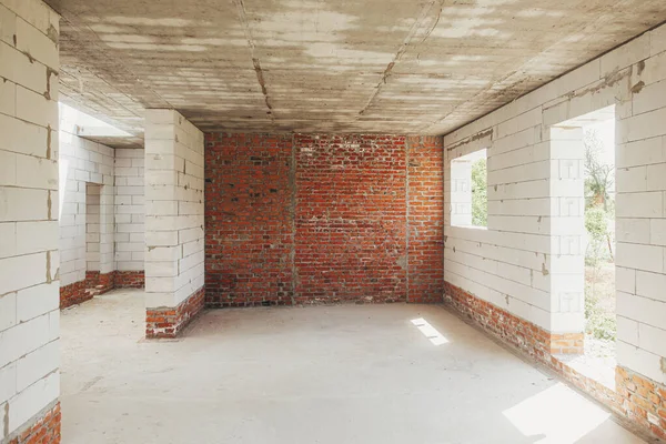 Unfinished house inside. Aerated concrete blocks and brick walls with windows, doorways and concrete floor. Process of house building at construction site. New house construction