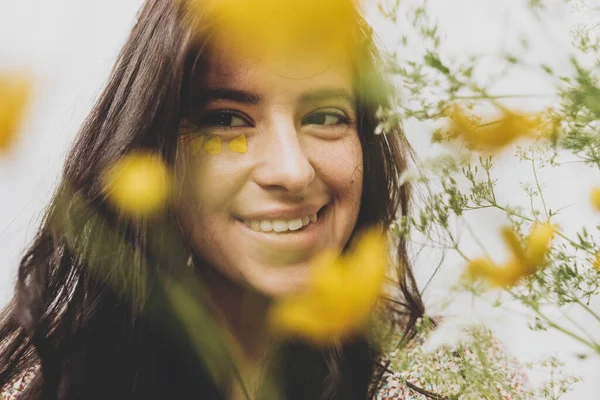 日当たりの良い部屋で野の花でポーズを目の下に黄色の花弁を持つ美しい幸せな女性 花と笑顔Bohoドレスで若いブルネットの女性の肖像画 スキンケアとセルフケア 夏気分 — ストック写真