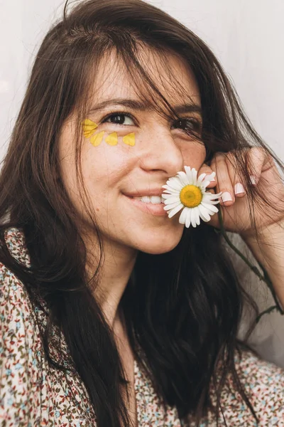 目の下に黄色の花弁を持つ美しい幸せな女性は日当たりの良い部屋にポーズ デイジーの花と笑顔Bohoドレスで若いブルネットの女性の肖像画 エイジングケアとセルフケア — ストック写真