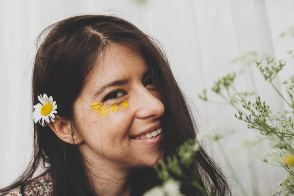 日当たりの良い部屋で野の花でポーズを目の下に黄色の花弁を持つ美しい幸せな女性 花と笑顔Bohoドレスで若いブルネットの女性の肖像画 スキンケアとセルフケア 夏気分 — ストック写真