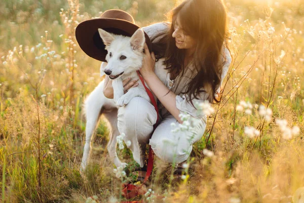 Stylowa Szczęśliwa Kobieta Gra Cute Dog Kapeluszem Wśród Dzikich Kwiatów — Zdjęcie stockowe