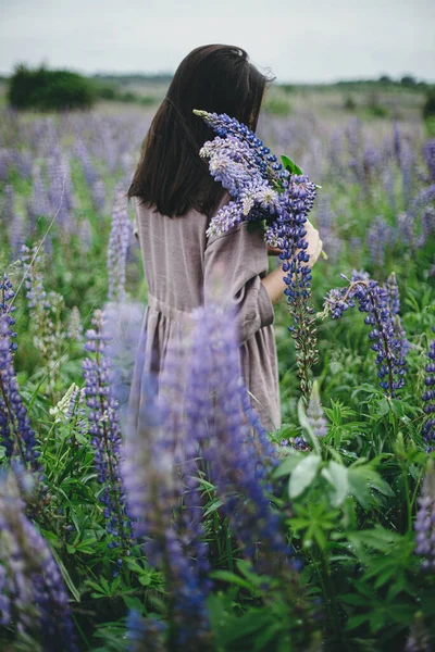 土工布美学 穿着乡村服装的时髦女人在草地上拿着丁香花束 穿着亚麻布衣服的年轻女性在夏日的乡间采摘野花 乡村生活缓慢 — 图库照片