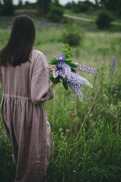 穿着乡村服装的时髦女人在草地上拿着丁香花束 土工布美学 穿着亚麻布衣服的年轻女性在夏日的乡间采摘野花 乡村生活缓慢 — 图库照片