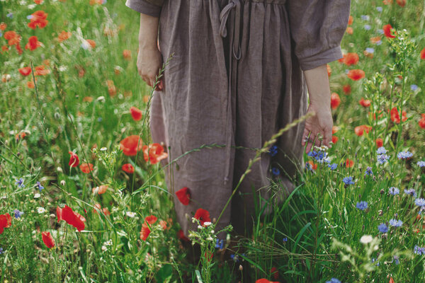 Cottagecore aesthetics. Close up of woman in rustic dress gathering poppy and cornflowers in sunny field. Young female walking among wildflowers meadow in summer countryside, slow life