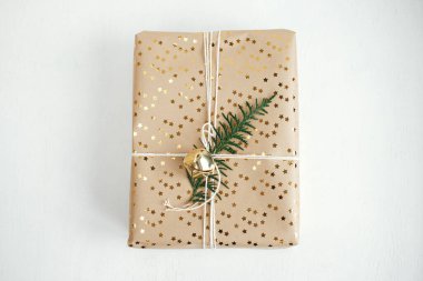Stylish christmas gift flat lay. Modern christmas gift box with fir branch, golden bell and festive paper composition on white wood with copy space. Merry Christmas and Happy Holidays!