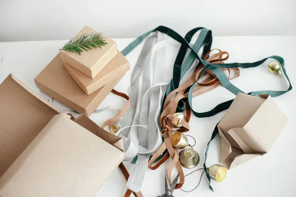 Wrapping stylish eco christmas gifts composition. Simple craft gift boxes, velvet ribbons, christmas bells, fir branch and scissors on white background. Merry Christmas! Sustainable holidays