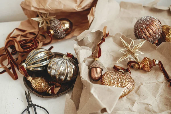 Merry Christmas! Stylish vintage christmas ornaments. Golden baubles, craft paper, ribbons and scissors on rustic white table. Moody banner. Preparation for winter holidays, atmospheric time