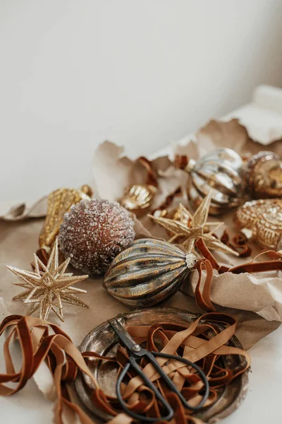 Stylish vintage christmas ornaments. Golden baubles, craft paper, ribbons and scissors on rustic white table. Merry Christmas! Moody banner. Preparation for winter holidays, atmospheric time