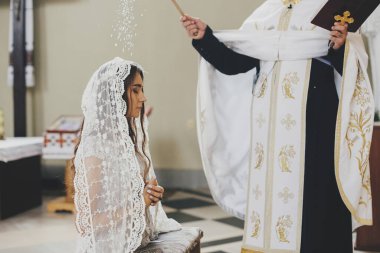 Rahip kutsal su ile kutsanmış şık gelin kilisede kutsal evlilik sırasında mihrapta. Katedralde düğün töreni. Klasik ruhani gelin duası.