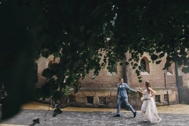 Gelin ve damadın ağaç yaprakları altında kilisenin arka planında koşup gülümsemesi. Provence düğünü. Avrupa 'nın en güzel duygusal çifti.