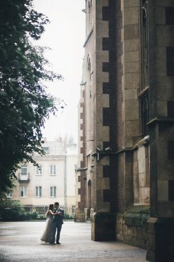 Yağmur Sokağındaki eski kilisenin arka planında dans eden şık gelin ve damat. Provence düğünü. Avrupa 'da yağmurda kucaklaşan güzel duygusal düğün çifti.