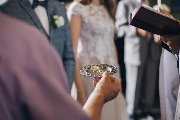神聖な結婚式のための教会でスタイリッシュな結婚指輪と司祭保持プレート 大聖堂での結婚式 花嫁と新郎の結婚指輪 — ストック写真