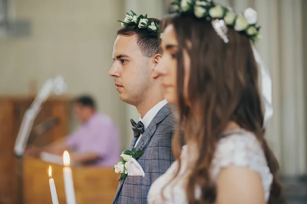 教会で聖なる結婚式の間にろうそくを保持する花冠のスタイリッシュな花嫁と新郎 大聖堂での結婚式 古典的な精神的な結婚式のカップル燃焼現代のキャンドル — ストック写真