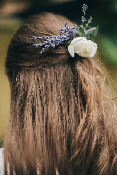 Beautiful lavender and rose flowers in bride hair close up. Stylish bride hairstyle with lavender flowers for provence wedding. Long hair with floral accessories