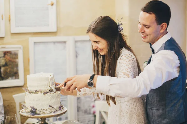スタイリッシュなレストランでラベンダーと現代的なケーキを一緒に切断スタイリッシュな幸せな結婚式のカップル プロバンス結婚式のレセプション おいしいウェディングケーキで祝う美しい花嫁と新郎 — ストック写真