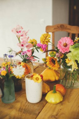 Autumn composition on rustic table. Colorful autumn flowers in vase, pumpkins and pattypan squashes on rustic wooden table. Harvest time in countryside. Hello Fall