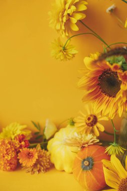 Stylish autumn composition. Colorful flowers, pumpkin, pattypan squash on yellow background. Creative modern autumnal still life. Seasons greeting card template with space for text. Hello Fall