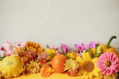 Stylish autumn composition with colorful autumn flowers, pumpkin, pattypan squash on yellow paper against rustic background. Happy Thanksgiving! Seasons greeting card template with space for text