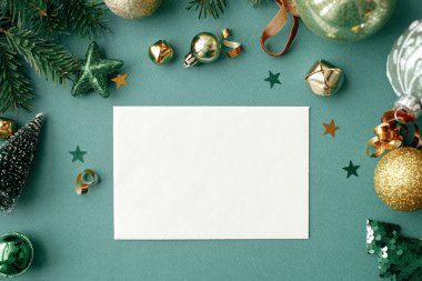 Christmas card flat lay. Modern greeting card mock up with stylish christmas decorations, fir branches, gold ornaments on green background. Empty postcard template, space for text. Merry Christmas!