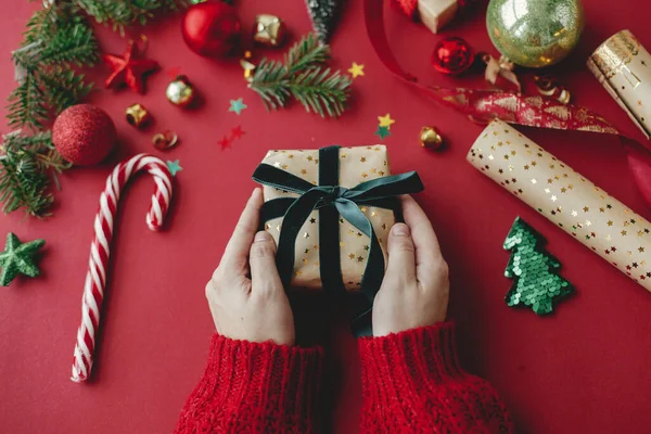 メリークリスマス 赤い背景にスタイリッシュなクリスマスギフト 黄金の包装紙 リボンやお祝いの装飾を保持する手 季節の挨拶だ ハッピー ホリデー — ストック写真