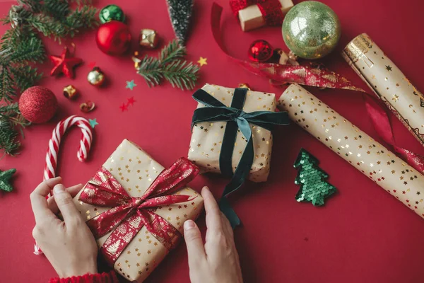 メリークリスマス 赤い背景にスタイリッシュなクリスマスギフト 黄金の包装紙 リボンやお祝いの装飾を保持する手 季節の挨拶だ ハッピー ホリデー — ストック写真