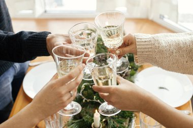 Noel ziyafeti. Şarap kadehli eller arka planda altın ışıklı ve mumlu köknar dalları olan şık masa ortamında kadeh kaldırıyor ve tıklıyor. Arkadaşlar şampanyayla kutlama yapıyor