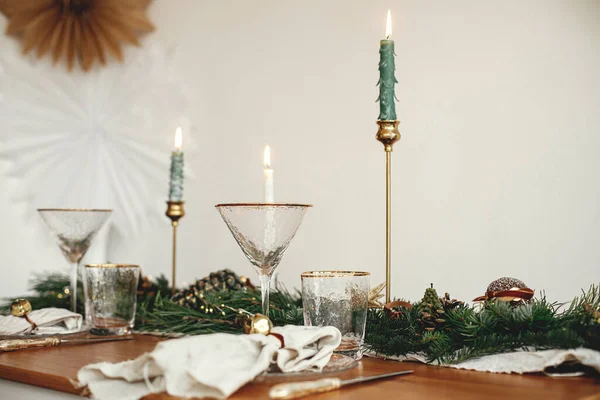Stylish Christmas table setting. Linen napkin with bell on plate, vintage cutlery, wineglass, fir branches with golden lights, pine cones and candle on table. Atmospheric Holiday brunch