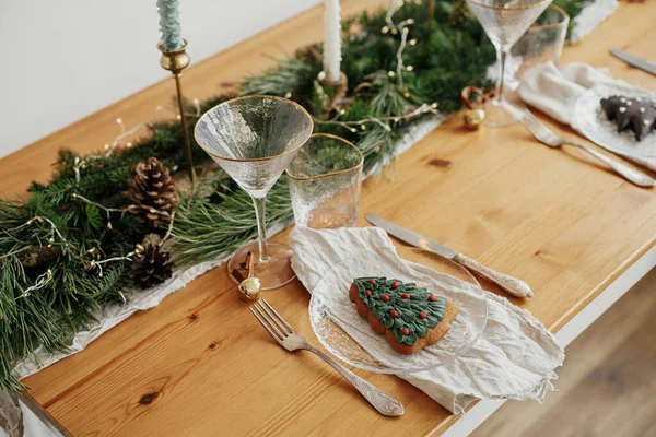 スタイリッシュなクリスマステーブルの設定 プレート上のクリスマスツリークッキー 鐘とリネンナプキン ヴィンテージカトラリー ワイングラス 金色のライトを持つモミの枝 テーブルの上のキャンドル 大気の休日ブランチ — ストック写真