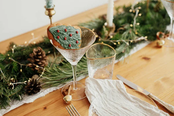 クリスマステーブルのセッティング ガラスのクリスマスツリークッキー リネンナプキンのプレート ヴィンテージのカトラリー 黄金のライトとテーブルの上に松のコーンとモミの枝 創造的な休日の配置 — ストック写真