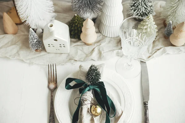 クリスマステーブルのセッティング プレート上のリボンと鐘を持つスタイリッシュなナプキン ヴィンテージのカトラリー モダンなお祝いのクリスマスツリーや白素朴なテーブルの上の家 テーブルの休日の配置 トップビュー — ストック写真
