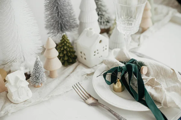 クリスマステーブルのセッティング プレート上のリボンと鐘を持つスタイリッシュなナプキン ヴィンテージのカトラリー モダンなお祝いのクリスマスツリーや白素朴なテーブルの上の家 テーブルの休日の配置 — ストック写真