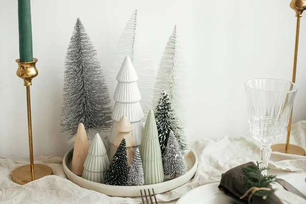スタイリッシュなクリスマステーブルの設定 プレート上の鐘とモミの綿のナプキン ヴィンテージカトラリー ワイングラス モダンなクリスマスツリーと白い素朴なテーブルの上にキャンドル 休日ブランチ — ストック写真