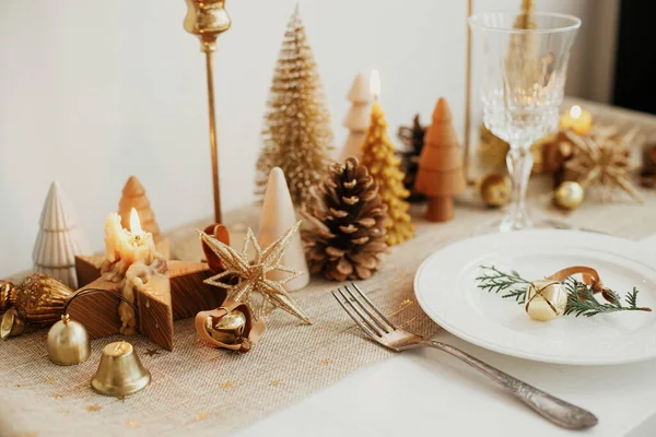 クリスマスの豪華なテーブルの設定 板の上に鐘を持つ杉の枝 ヴィンテージカトラリー 黄金の小さなクリスマスツリーやテーブルの上の装飾品 テーブルの休日の配置 — ストック写真