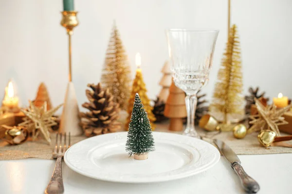 クリスマスの豪華なテーブルの設定 プレート上の鐘 ヴィンテージカトラリー ガラス テーブルの上に金色の小さなクリスマスツリーや装飾品を持つ小さなクリスマスツリー テーブルの休日の配置 — ストック写真