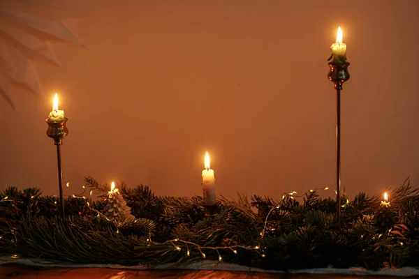 テーブルの上の夜暗い部屋でモミの枝や黄金のライトとスタイリッシュなクリスマスキャンドル 大気中のクリスマスや新年の前夜 黄金のライトと松の装飾とムーディーナイト画像 — ストック写真