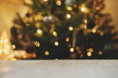 Tahta masa, Noel ağacının arka planında, altın ışıklı bokeh. Noel şablonu ve ürün için maket. Aydınlatılmış ağaçlı festival odasına karşı beyaz ahşap tahta